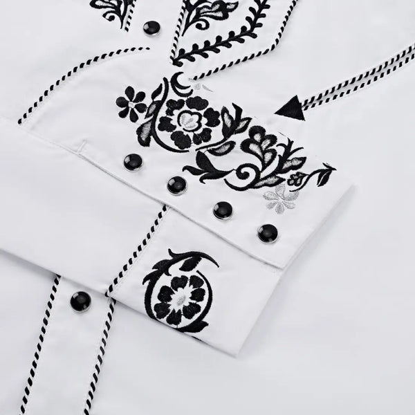 Close-up of the white western shirt cuff showing black floral embroidery, black snap buttons, and contrast piping trim