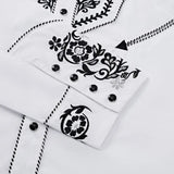Close-up of the white western shirt cuff showing black floral embroidery, black snap buttons, and contrast piping trim